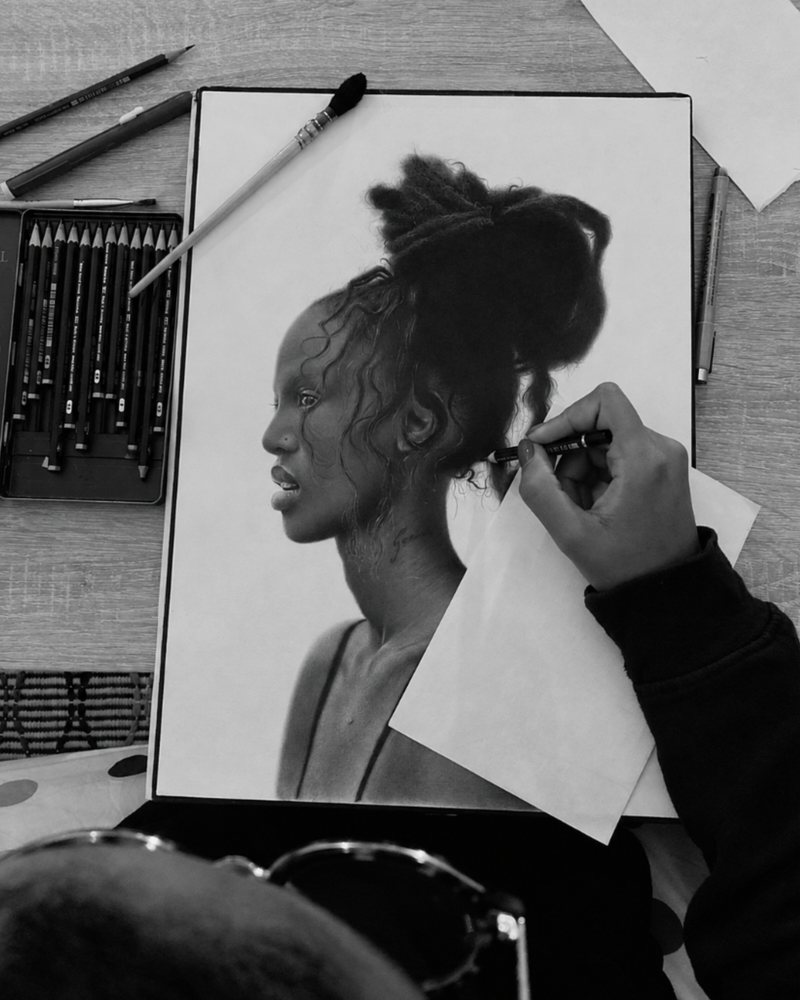 La Couronne in progress: a hand shading the hair, a box of graphite pencils open on the table.
